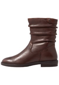 Brun läderankelsko med en slokad design, slät yta, låg klack och enkel sömdekoration, med en liten accentknapp.