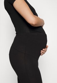 Leggings de maternité noirs avec une taille haute, un design sans couture et une texture douce, présentés sur fond neutre avec un profil latéral.