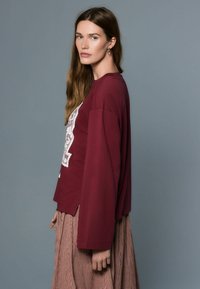 Tumepunane pikkade varrukatega särgi esiküljel on pitsdetailid, mida on kombineeritud ruudulise seelikuga. Pehme kangas ja lõõgastav istuvus küljetel lõhikutega.