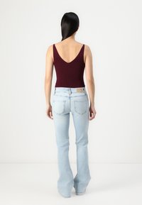 Body bordeaux côtelé avec un décolleté en V profond, associé à un jean évasé bleu clair avec une étiquette de marque au dos et des poches discrètes à l'arrière.