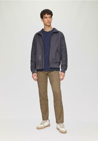 Mannelijke casual outfit met een donkergrijze jas, marineblauwe shirt, khaki broek en witte sneakers met beige accenten. Gladde stof met een minimalistisch ontwerp.