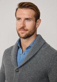 Cárdigan de punto gris con cuello tipo chal, que presenta un patrón texturizado y cierre de botones, llevado sobre una camisa azul clara.