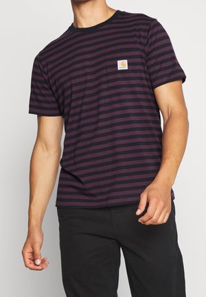 Homme portant un t-shirt à manches courtes rayé violet foncé et noir avec le logo Carhartt sur la poche poitrine et un pantalon noir, debout devant un fond blanc.