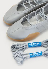 Lysegrå skinnsko med brune gummisåler, kryssede lisser og to ekstra par Adidas grå skolisser med blå etiketter.