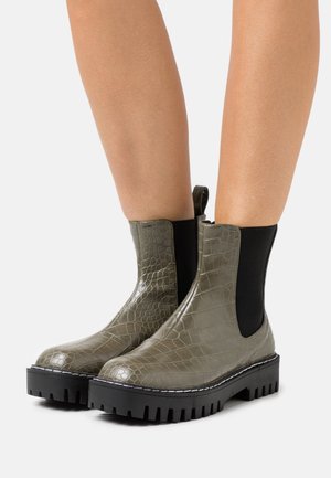 Grüne Chelsea-Stiefel aus Kroko-Prägung mit schwarzen elastischen Einsätzen und dicken schwarzen Gummisohlen mit tiefem Profil für besseren Halt.