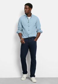 Hellblaues Hemd mit Knopfverschluss aus strukturiertem Stoff, kombiniert mit dunkelblauen Jeans und weißen Sneakers. Lässige, gut sitzende Kleidung.