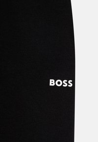 Schwarzer Baumwollstoff mit gerippter Textur und prominentem weißen "BOSS"-Logo, das an der Seite aufgedruckt ist.