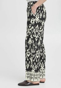 Pantalons à motif noir et crème avec une taille élastique, des poches latérales et une bordure décorative au bas. Tissu lisse et léger.