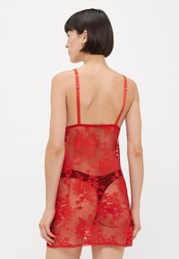 Red lace chemise featuring adjustable straps, sheer floral pattern, scalloped hem, and matching lace thong, designed for a fitted silhouette.