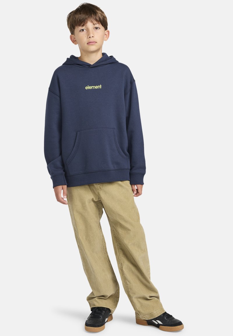 Navyblå sweatshirt med ficka fram, ribbad mudd och en neongrön logga. Matchad med lösa beiga kordbyxor och svarta sneakers.