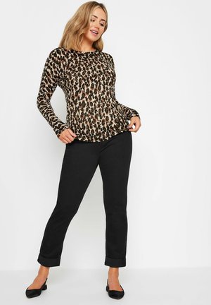 Langarmshirt im Leopardenmuster in Beige- und Schwarztönen, kombiniert mit schwarzen Rollcuff-Hosen und schwarzen Schuhen. Glatte Stoffoberfläche.