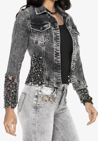 Musta farkkutakki kirjailtuin hihoin, metallisin yksityiskohdin ja kulutuksin. Yhdistetty harmaiden farkkujen kanssa, joissa on jalokivikoristeet.