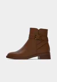 Smeđa kožna gležnjača s niskom slojevitom petom, detaljem kopče na remenu oko gležnja i glatkim završetkom. Bočni patentni zatvarač za jednostavno nošenje.