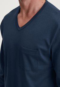Navy blauwe longsleeve t-shirt met een V-hals, met een gestikte zak op de linkerborst en een zachte, gelijkmatige textuur.