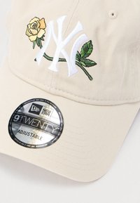 Bézs színű baseball sapka állítható mérettel. Fehér hímzett NY logóval és sárga rózsa mintával zöld levelekkel. New Era 9TWENTY címkével ellátva.