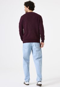 Bordeaux gebreide trui met geribbelde manchetten en zoom, gecombineerd met lichtblauwe, loszittende jeans en witte sneakers met zwarte strepen.