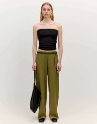 Zwarte geribbelde strapless top gecombineerd met olijfgroene wijde broek; houdt een zwarte handtas vast; rechthoekige vorm met verticalen lijnen.