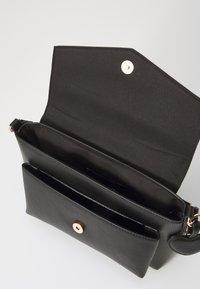 Sac à main en cuir noir avec une surface texturée, des accessoires en or et une fermeture rabat. L'intérieur présente une doublure noire et plusieurs compartiments.