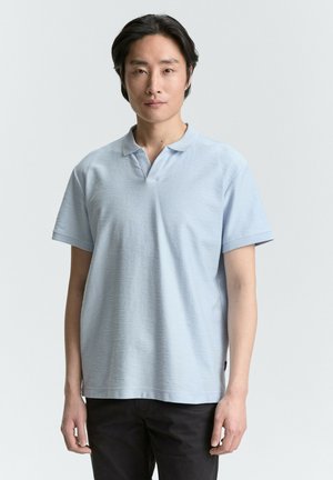 Polo de culoare albastru deschis, realizat dintr-un material texturat, având un guler scurt și mâneci scurte, asortat cu pantaloni negri. Design minimal.