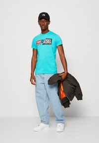 Turquoise t-shirt with black and red Diesel logo, light blue jeans, and black bomber jacket with orange lining, white sneakers.