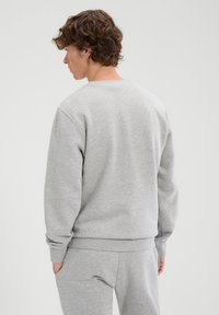 Sudadera gris con cuello redondo, mangas largas y puños acanalados. Hecha de material suave, con un diseño simple y sin adornos.