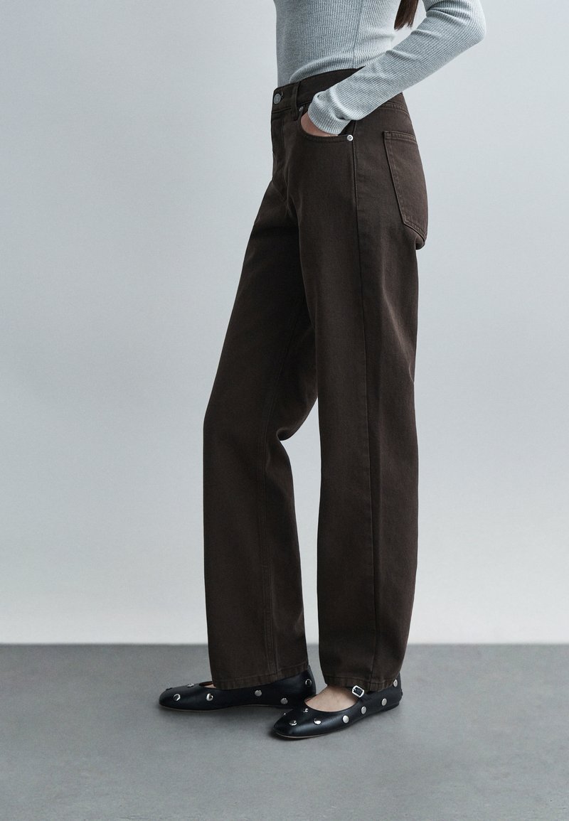 Magas derekú barna farmernadrág egyenes szárú szabással, két zsebbel és kontrasztos varrással, fekete balerinacipővel párosítva.