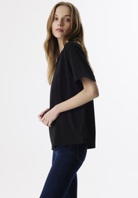 Zwart T-shirt met korte mouwen, een relaxte pasvorm, ronde halslijn en zachte textuur, gecombineerd met donkerblauwe slim fit jeans.