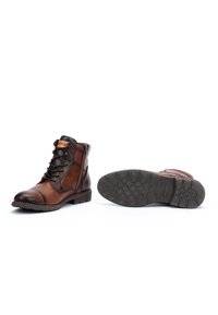 Botas de hombre de cuero marrón con cordones negros, cremallera lateral y suelas de goma texturizadas, exhibidas sobre un fondo blanco.