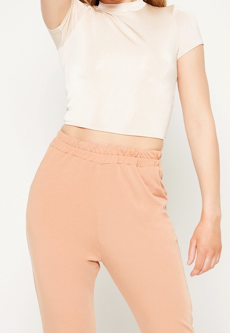 Světle béžový crop top s krátkými rukávy, který má hladkou texturu. Broskvové teplákové kalhoty s elastickým pasem a bočními kapsami.