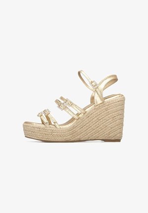 Sandalia de cuña dorada con tres correas, con detalles de piedras preciosas; plataforma de textura tejida; punta redondeada; correa ajustable en el tobillo.