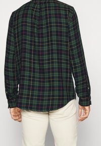 Green plaid shirt with navy, red, and yellow lines, featuring a button-down collar and long sleeves, shown from the back against a white background.