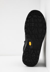 Černá venkovní podrážka boty s hlubokými, robustními vzorky. Obsahuje žluté logo Vibram a texturovanou gumu pro lepší přilnavost a odolnost.
