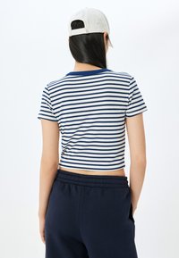 Kort top med marineblå og hvide striber, ribbet tekstur og marineblå halsudskæring, parret med marineblå sweatpants og en lys kasket.