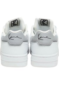 Hvite sneakers med en glatt skinnøvre, grå detaljer på hælen og en svart logo. Signaturdetalj bak. Polstret krage.