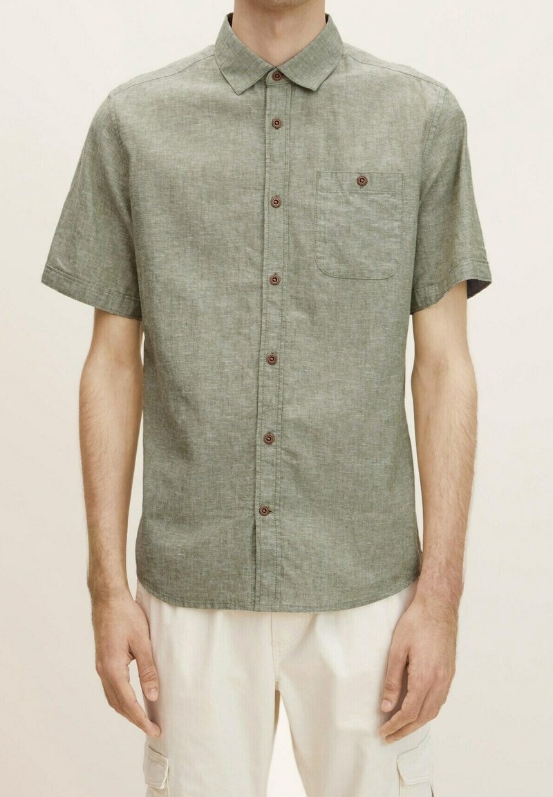 Camisa de lino mezclado verde de manga corta con cuello abotonado, botones marrones y bolsillo en el pecho. Textura suave, corte casual.