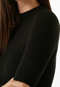 Pull noir en maille côtelée avec un col montant et des manches longues ajustées. La texture est lisse avec des lignes verticales, soulignant une coupe près du corps.