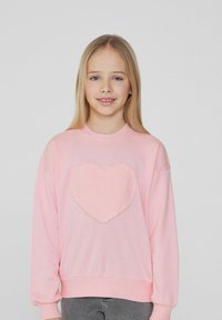 Růžová bavlněná mikina s texturovanou aplikací srdce ve středu, volný střih, dlouhé rukávy a žebrované manžety.