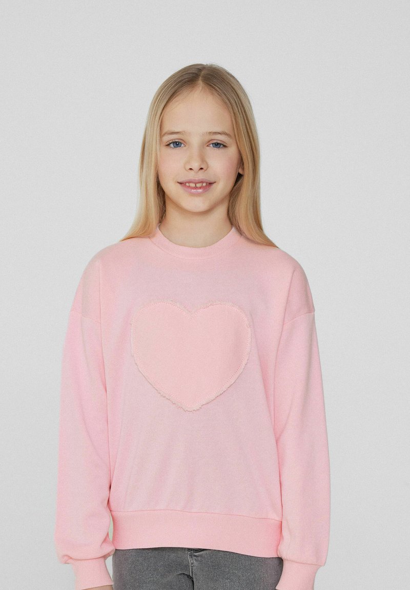 Růžová bavlněná mikina s texturovanou aplikací srdce ve středu, volný střih, dlouhé rukávy a žebrované manžety.