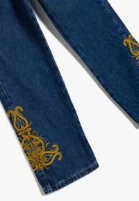 Mörkblå denimjeans med intrikata gula broderier längs fållen, med en strukturerad form och standardstygn.