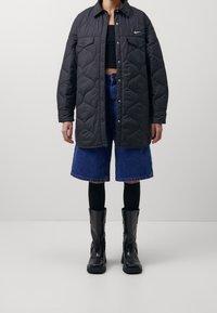 Svart quiltad jacka med tryckknappar, två bröstfickor; kombinerad med högmidjade denimshorts och svarta knähöga stövlar.