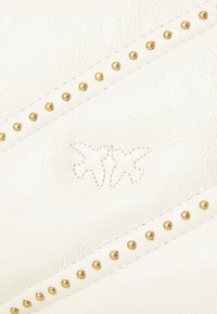 Sac à main en cuir blanc avec des clous en métal doré, des motifs de couture diagonaux et un design embossé de deux oiseaux. Texture lisse.