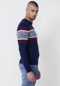 Jersey azul marino con patrón a rayas en gris y granate, cuello redondo y mangas largas. Textura suave con puños y dobladillo acanalados.