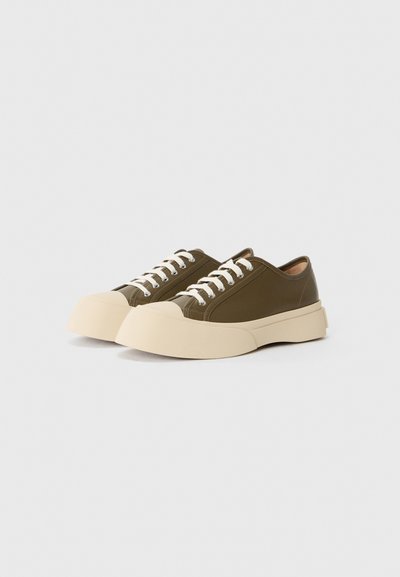 Olive green sneakers with a beige rubber sole and white laces, featured against a plain, light background.