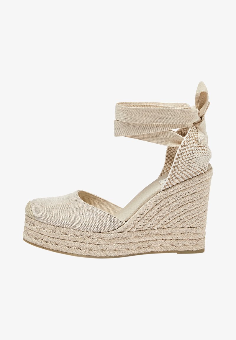 Espadrilles à talons compensés beiges avec un upper en texture tissée et des sangles de cheville. Le talon présente des détails en jute tressé, ajoutant un aspect naturel.