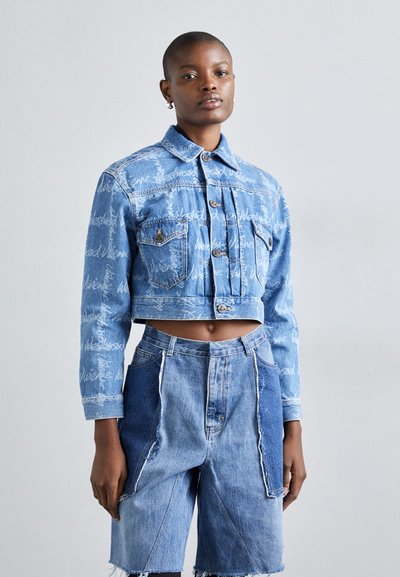 Jachetă din denim scurtă, cu buzunare frontale, de culoare albastră cu text alb imprimat, asortată cu pantaloni scurți din denim cu talie înaltă, cu design patchwork și margini desfăcute.