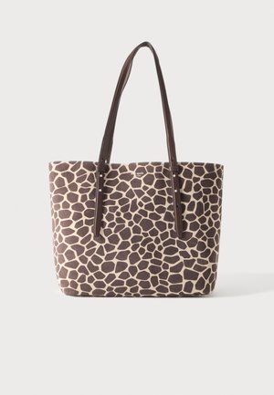 Sac tote avec un motif imprimé girafe irrégulier marron et beige et des bretelles en cuir marron foncé sur un fond uni.