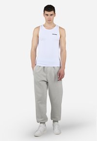 Top blanco sin mangas con logo negro, combinado con pantalones de chándal de felpa gris claro. Los pantalones tienen puños elásticos y bolsillos laterales, llevados con zapatillas blancas.