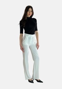 Zwart, kort mouw turtleneck top gecombineerd met strakke, high-waisted witte broeken. De broeken hebben zijzakken; de schoenen zijn zwarte puntige hakken.