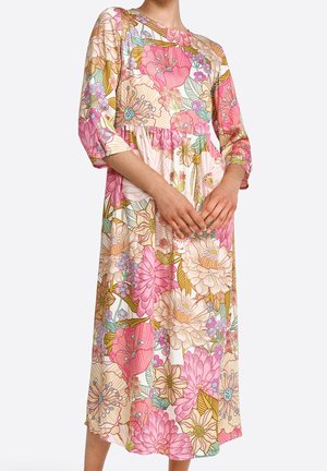 Mujer con un vestido midi de manga larga con grandes estampados florales en rosa, beige y verde y una cintura fruncida.