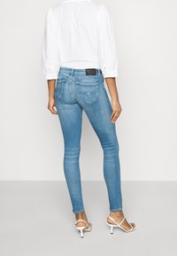 Tajta jeans i ljust blånande denim, med en midjehöjd i medelhöjd, två bakfickor och en svart logotyp vid midjan.